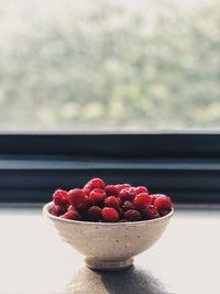 Close-up of raspberries in bowl on table against window
