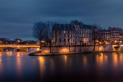 Illuminated bridge over river by buildings against sky at night