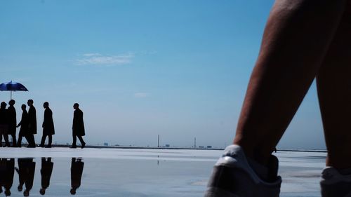 Men walking at beach against blue sky