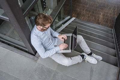 Man using laptop sitting on stairs in office