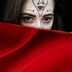 Close-up portrait of young woman with face paint and red fabric