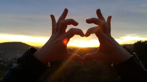 Cropped hands making heart shape against sky