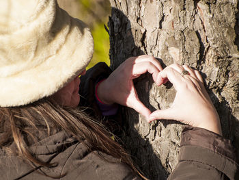 Woman making heart shape on tree trunk