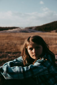 Side view portrait of girl sitting on field against sky