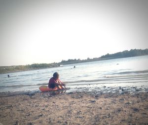 Man sitting on beach against clear sky