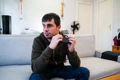 Male with eyesight disability scrolling mobile phone while sitting on couch at home