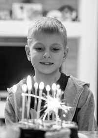 Cute boy looking at lit candles on birthday cake at home