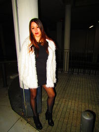 Portrait of young woman standing against wall at night