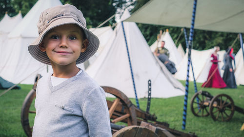 Portrait of boy wearing hat standing against tents
