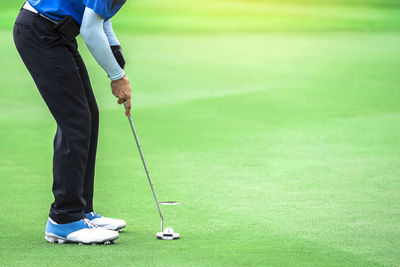 Low section of person holding ball while standing on grass