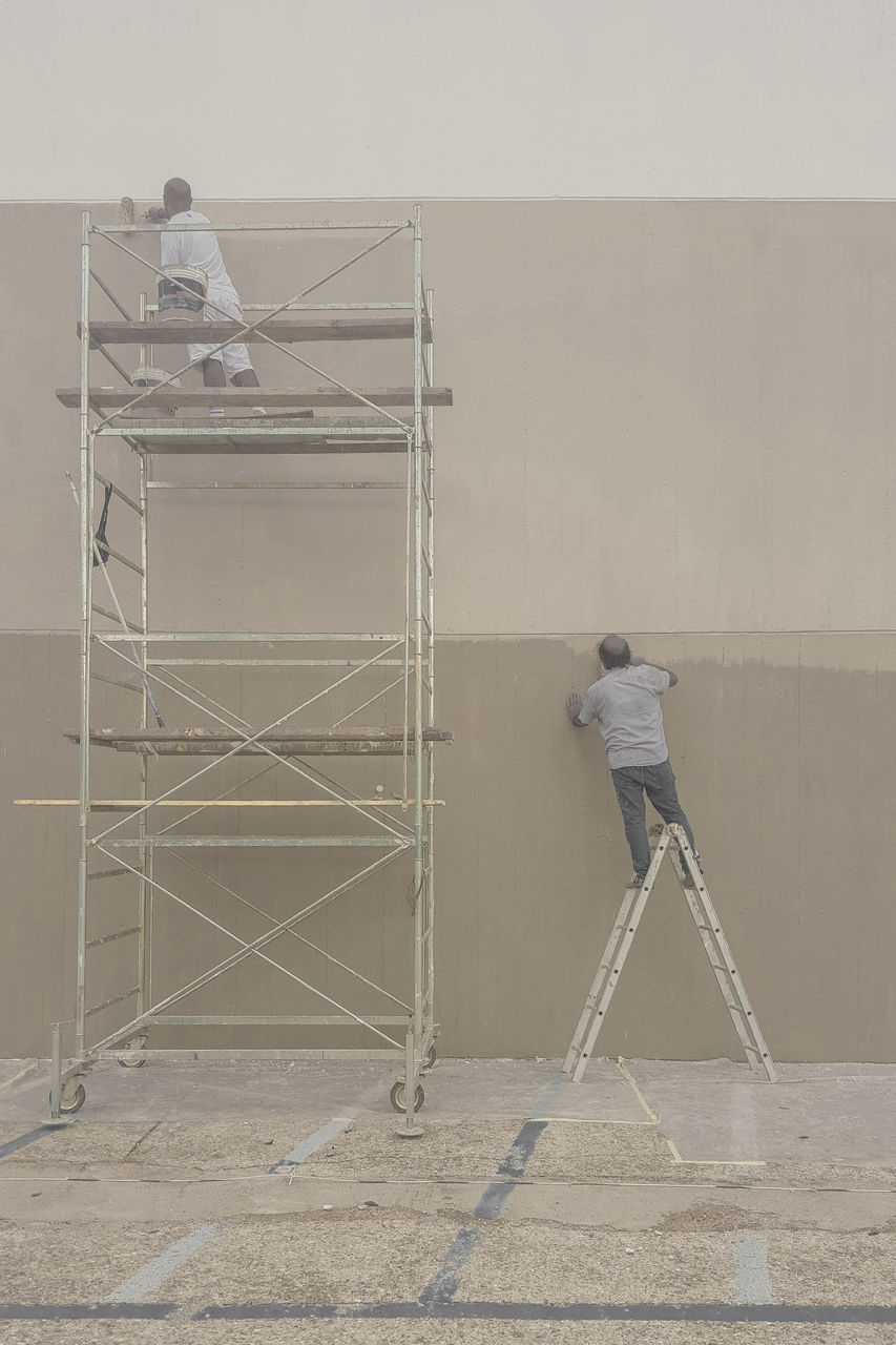 REAR VIEW OF MAN WORKING ON WALL