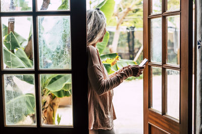 Side view of woman using phone while standing at entrance of home