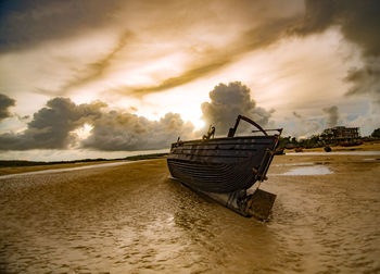 Boat moored on shore against sky during sunset