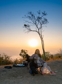Rear view of man sitting on field against sky during sunset