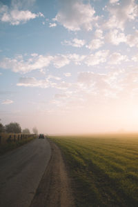 Road by agricultural field against sky during sunset