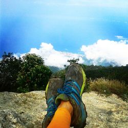 Low section of woman wearing shoes against blue sky