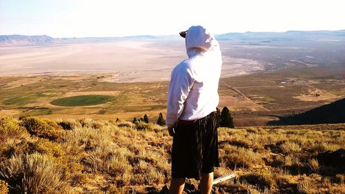 Rear view of man looking at landscape from mountain during sunny day