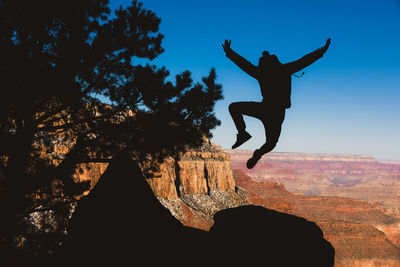 Silhouette man jumping on rock against sky