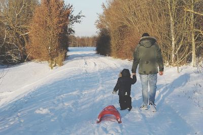 Rear view of man with son holding sled walking on snow covered road