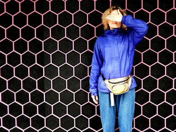 Woman standing by fence against blue wall