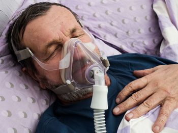 High angle view of senior man with oxygen mask sleeping on bed