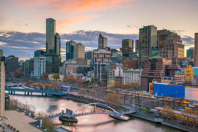 Bridge over river amidst buildings against sky during sunset