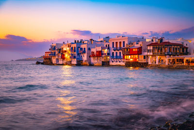 Buildings by river against sky during sunset