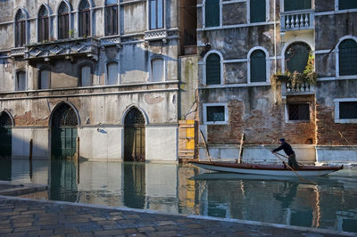 Man oaring boat in canal against building