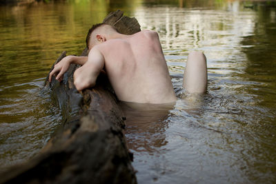 Rear view of naked man sitting in river