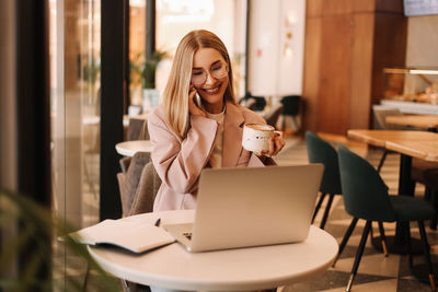 A millennial woman with glasses works and studies online using a mobile phone and technology in cafe