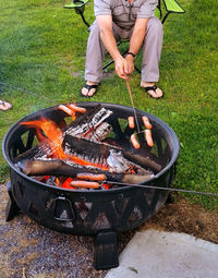 Low section of man roasting sausages over fire pit