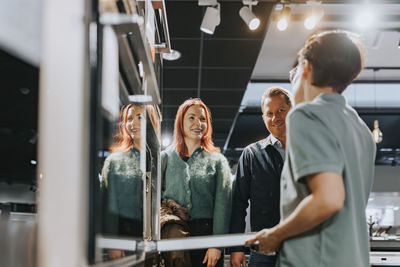 Happy couple looking at saleswoman assisting in buying microwave oven at electronics store