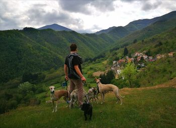 Full length of man standing with dogs on mountain against sky