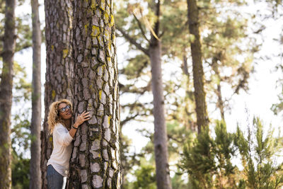 Side view of mature woman hugging tree trunk in forest