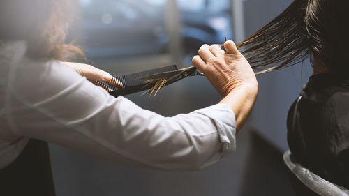 Midsection of hairdresser cutting woman hair at salon