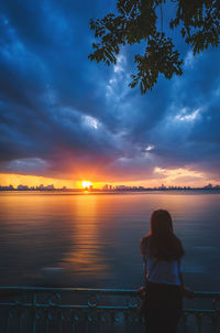 Silhouette woman standing by sea against sky during sunset