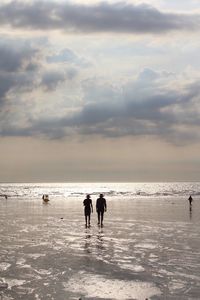 Silhouette people on shore at beach against sky during sunset