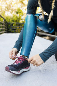 Athlete tying shoelace of prosthetic leg shoe on bridge