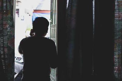 Rear view of man talking on mobile phone while standing at home