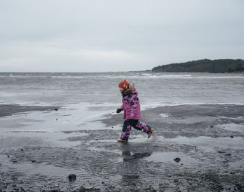 Girl in pink winter clothes running on muddy beach