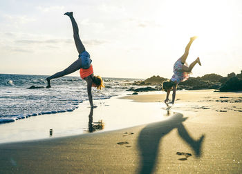 People doing handstand at beach against sky