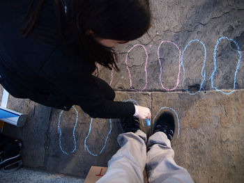 Low section of man standing while woman drawing shoe shapes on street