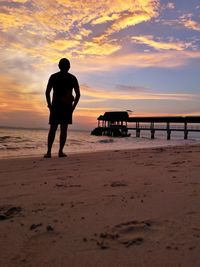 Rear view of silhouette man looking at sea against dramatic sky during sunset