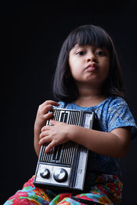 Portrait of cute girl holding radio against black background