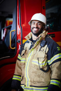 Portrait of smiling male firefighter standing against fire engine at fire station