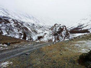 Snow covered road by mountain against sky