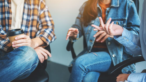 Low section of friends using digital tablet while sitting on sofa at home