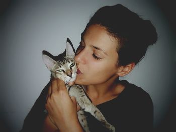 Portrait of young woman with cat sitting against gray background