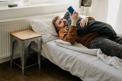 Lazy man using phone while lying on bed at home