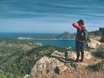Traveler woman shadowing eyes while watching blue sea bay within mountain single trail